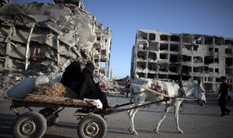 Warga Jalur Gaza menaiki keledai diengan latar belakang gedung yang hancur dibombardir militer Israel.