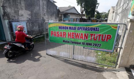 Warga melewati pintu gerbang pasar hewan Muning yang ditutup sementara di Kota Kediri, Jawa Timur, Jumat (10/6/2022). Pemerintah daerah Kota Kediri memperpanjang penutupan pasar hewan dari sebelumnya dua pekan menjadi selama empat pekan guna menangkal penyebaran penyakit mulut dan kuku (PMK) pada hewan ternak.