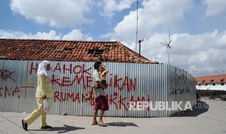   Warga melintas berlatar penolakan pengusuran di kawasan Luar Batang, Penjaringan, Jakarta Utara , Selasa (5/3).(Republika/Tahta Aidilla)