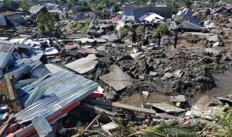 Warga melintas di antara reruntuhan rumah di Perumnas Bala Roa, Palu, Ahad (30/9). BNPB merilis 420 korban meninggal dunia akibat gempa bumi yang melanda Kota Palu hingga Sabtu (29/9) malam. 