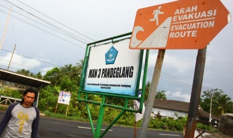 Warga melintas di bawah papan petunjuk arah evakuasi bencana tsunami yang ada di kawasan Panimbang, Pandeglang, Banten, Selasa (25/12/2018).