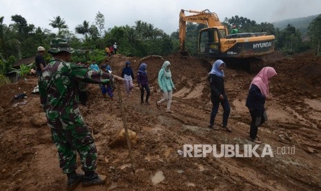 Warga melintas di depan alat berat yang tengah mencari korban longsor di Desa Banaran, Kecamatan Pulung, Kabupaten Ponorogo, Jawa Timur, Kamis (6/4).