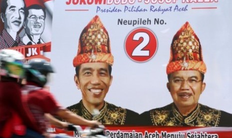 Warga melintas di depan alat peraga kampanye (APK) pasangan capres cawapres Jokowi - Jusuf Kalla yang memakai pakaian adat Aceh di Kota Lhokseumawe, Aceh, Senin (23/6). 