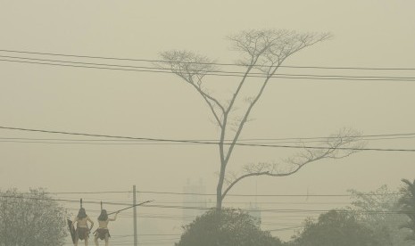 Warga melintas di depan patung orang dayak yang masih diselimuti asap di Palangkaraya, Kalimantan Tengah, Kamis (1/10).