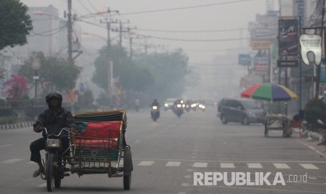 Warga melintas di jalan yang berkabut asap dari kebakaran hutan dan lahan di Kota Dumai, Dumai, Riau, Jumat (15/2/2019). 