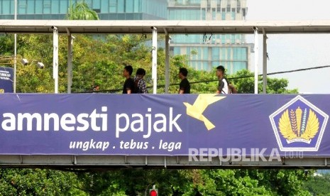 Warga melintas di jembatan penyebrangan orang (JPO) yang terpasang spanduk sosialisai pengampunan pajak di kawasan Stasiun Gambir, Jakara, Ahad (31/7).  (Republika/ Agung Supriyanto)