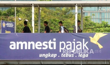 Warga melintas di jembatan penyeberangan orang (JPO) yang terpasang spanduk sosialisasi pengampunan pajak di kawasan Stasiun Gambir, Jakara.  (Republika/ Agung Supriyanto)