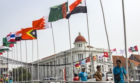 Warga melintas di samping deretan bendera negara peserta Asian Games 2018 yang dipasang di kawasan Kali Besar, Kota Tua, Jakarta, Kamis (19/7). 