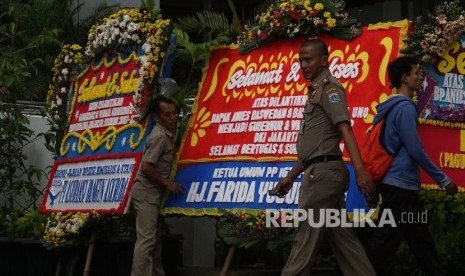 Warga melintas disamping karangan bunga yang berisi ucapan selamat kepada Anies Baswedan dan Sandiaga Uno di Balai Kota DKI Jakarta, Senin (16/10).