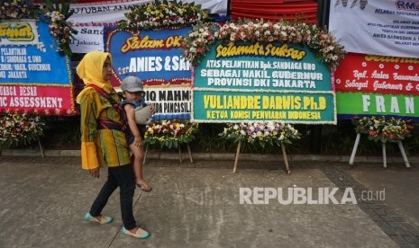 Warga melintas disamping karangan bunga yang berisi ucapan selamat kepada Anies Baswedan dan Sandiaga Uno di Balai Kota DKI Jakarta, Senin (16/10).