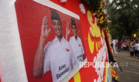 Warga melintas disamping karangan bunga yang berisi ucapan selamat kepada Anies Baswedan dan Sandiaga Uno di Balai Kota DKI Jakarta, Senin (16/10).