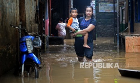 Seorang ibu menggendong anaknya melintasi banjir akibat luapan sungai Ciliwung di Kebon Pala II, Jakarta, Senin (13/2). 