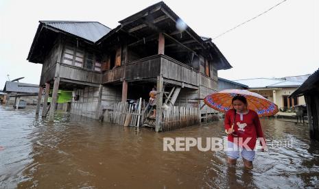 Warga melintasi banjir luapan Sungai Lempur yang menggenangi kawasan permukiman di Lempur Tengah, Gunung Raya, Kerinci, Jambi, Jumat (17/12/2021). Warga setempat menyebutkan kawasan permukiman di tepi aliran Sungai Lempur tersebut telah mengalami empat kali banjir dalam seminggu terakhir yang diduga akibat bertambah maraknya aktivitas penebangan ilegal di bagian hulu sungai sejak dua tahun terakhir.