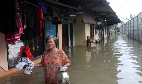 Warga melintasi banjir yang merendam kawasan permukiman Kampung Buaran, Harapan Mulya, Bekasi, Jawa Barat, Minggu (19/2). 