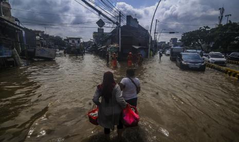 Warga melintasi genangan air saat terjadi banjir di Jalan Jatinegara Barat.