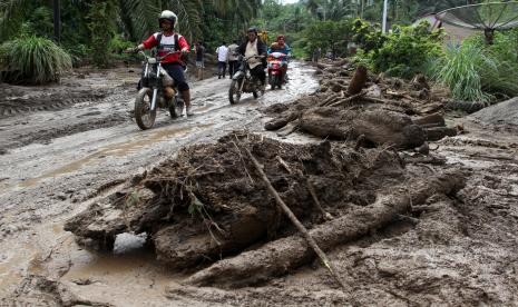 Warga melintasi jalan yang tertutup lumpur dari luapan Sungai Batang Nango di Kampung Sawah, Nagari Kajai, Kecamatan Talamau, Kabupaten Pasaman Barat, Sumatera Barat, Selasa (1/3/2022). Sebanyak tiga ton ikan larangan berjenis garing mati karena air Sungai Batang Lubuk Landur bercampur lumpur pascalongsor yang dipicu gempa magnitudo 6,1.