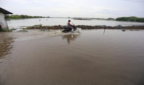 Warga melintasi ruas jalan raya Desa Karangsong, Kecamatan/Kabupaten Indramayu yang terendam banjir rob, Jumat (2/12/2022).