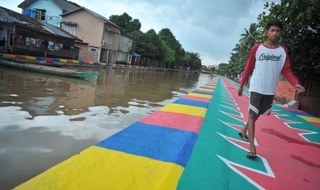 Warga melintasi tepian anak sungai yang telah dicat warna-wani di kawasan anak sungai Sekanak 26-27 Ilir Palembang, Sumsel, Selasa (9/1). Pemerintah Kota Palembang mengecat kawasan anak sungai ini menjadi menarik mata dalam rangka menyambut perhelatan olahraga Asian Games Agustus mendatang.