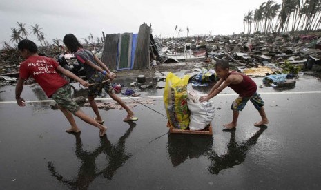   Warga membawa barang-barang bantuan melewati rumah yang hancur di kota Tacloban, Leyte provinsi Leyte, Filipina tengah, Ahad (10/11).  (AP/Bullit Marquez)