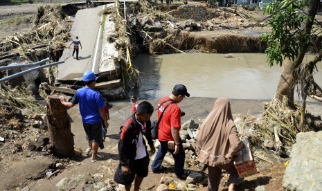 Warga membawa barang bawaannya melewati jembatan Kodo yang ambruk pascabanjir di Kelurahan Kodo, Kecamatan Rasana'e Timur, Kota Bima, NTB, Minggu (25/12).