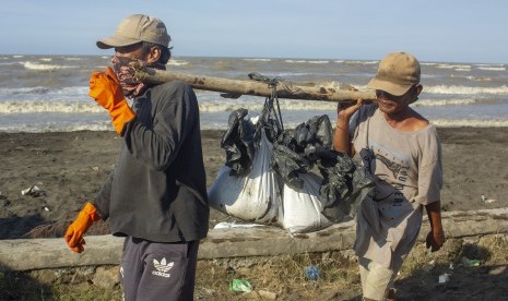 Warga membawa karung berisi pasir yang tercemar tumpahan minyak mentah (Oil Spill) di pesisir Pantai Cemarajaya, Karawang, Jawa Barat, Rabu (24/7/2019).