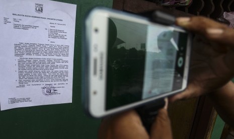 Warga memotret menggunakan telepon seluler surat pemberitahuan dari Pemprov DKI Jakarta yang tertempel di salah satu rumah di kawasan Kalijodo, Jakarta, Ahad (14/2). 