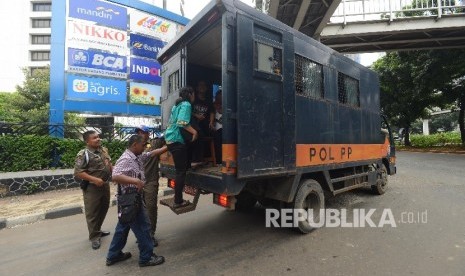 Warga menaiki mobil Satpol PP di Jalan Sudirman, Jakarta Pusat, Selasa (22/3).