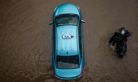 Warga mendorong motornya di dekat taksi yang terendam genangan banjir di Jalan DI Panjaitan, Cawang, Rabu (1/1/2020). Banjir tersebut disebabkan karena tingginya intensitas hujan yang mengguyur sejak Selasa (31/12/2019). 