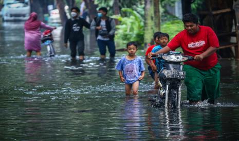 Warga mendorong motornya melintasi banjir. 