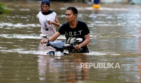 Warga mendorong sepeda motor melintasi banjir akibat air luapan Sungai Ciliwung, Bukit Duri, Jakarta, Kamis (16/2). 