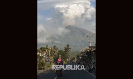 Warga mengendarai sepeda motor dengan latar belakang erupsi Gunung Agung di Desa Culik, Karangasem, Bali, Jumat (29/6).