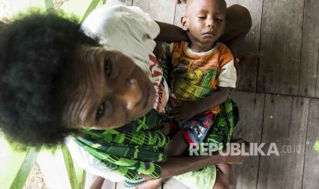 Warga menggendong anaknya saat menunggu antrean berobat di puskesmas Ayam di kampung Bayiwpinam, Distrik Akat, Kabupaten Asmat, Papua, Jumat (26/1).