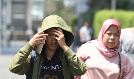 Warga menghalau sinar matahari dengan pakaiannya saat melakukan aktivitas di kawasan Bundaran Hotel Indonesia, Jakarta, Selasa (22/10/2019). 