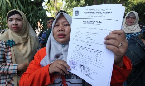 Warga menunjukkan Surat Hasil Ujian Sementara (SHUS) saat berunjukrasa di Balai Kota Surabaya, Jawa Timur, Rabu (19/6/2019). 