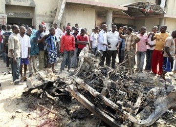 Warga menyaksikan bangkai mobil yang digunakan dalam aksi bom bunuh diri di dekat gereja Katholik St. Theresa di Madalla, Nigeria, Ahad (25/12). 