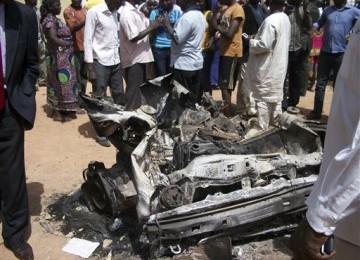 Warga menyaksikan bangkai mobil yang digunakan untuk aksi bom bunuh diri di sebuah Gereja Katholik di Jos, Nigeria, Ahad (11/3).