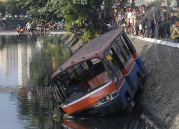 Warga menyaksikan metromini yang mengalami kecelakaan dan masuk nyebur kali. 