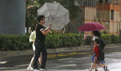 Warga menyeberang jalan di tengah tiupan angin kencang yang disebabkan oleh Topan Bailu di Taipei, Taiwan, Sabtu (24/8).