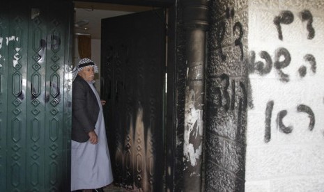 Warga Palestina berdiri dekkat pintu masjid di Deir Istiya Ramallah yang dibakar dan dicoret oleh ekstrimis Yahudi