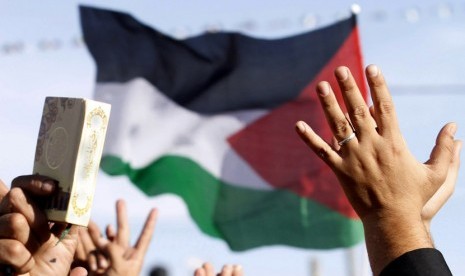 Warga Palestina mengibarkan bendera dan memegang kitab suci Alquran saat merayakan pengakuan negara Palestina oleh PBB di Ramallah,Ahad (2/12). (AP/Nasser Shiyoukhi)