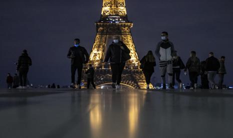 Warga Paris mengenakan masker berjalan di belakang Menara Eiffel. Prancis mencatat mencatat 12.489 kasus baru Covid-19 selama 24 jam terakhir. Ilustrasi.