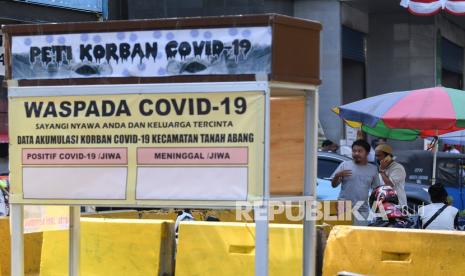 Warga tanpa mengenakan masker melintasi replika peti mati dan papan himbauan waspada COVID-19 