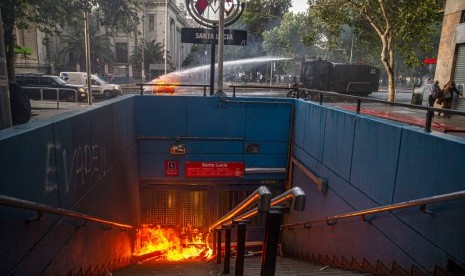 Water cannon polisi memadamkan barikade yang dibakar demonstran di stasiun kereta bawah tanah Santa Lucia di Santiago, Cile, Jumat (18/10).