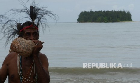 Wellem Kalami sedang meniup un untuk memgumpulkan warga, berlatar belakang Pulau Um. Warga berkumpul untuk membangun, tetapi tidak jika harus membabat hutan. 