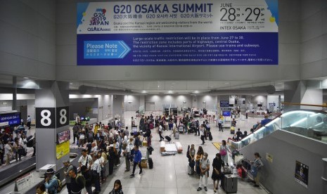 Wisatawan beraktivitas di bawah spanduk pengumuman pengalihan arus saat Pertemuan G20 mendatang, di Bandara Internasional Kansai, Osaka, Jepang, Senin (24/6/2019). 