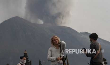 Wisatawan beraktivitas di Pura Besakih yang berlatar belakang Gunung Agung meletus di Karangasem, Bali, Selasa (28/11).