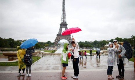 Wisatawan berfoto di pelantaran Trocadero dengan latar pemandangan Menara Eiffel saat hujan mengguyur Paris, Prancis. UNWTO mengatakan pandemi Covid-19 dapat menurunkan tingkat pariwisata internasional. Ilustrasi.