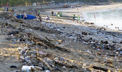 Wisatawan berjalan di antara tumpukan sampah yang terdampar di Pantai Kuta, Bali, Senin (15/2).