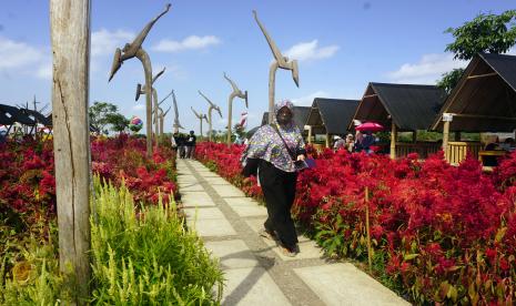 Wisatawan berjalan di tengah taman bunga dengan latar belakang patung keris di taman wisata Nakula Park, Desa Kendalbulur, Tulungagung, Jawa Timur, Ahad  (23/8/2020). Objek wisata rintisan berbasis desa dengan harga tiket Rp2 ribu per orang ini ramai dikunjungi wisatawan saat liburan akhir pekan.