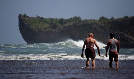 Wisatawan berjalan untuk mandi di laut saat berwisata di Pantai Baron, Gunung Kidul, Yogyakarta.